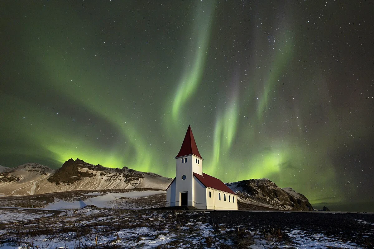 Fotomontage - Polarlicht über der Víkurkirkja Kirche von Vik in Island in einer klaren Nacht.